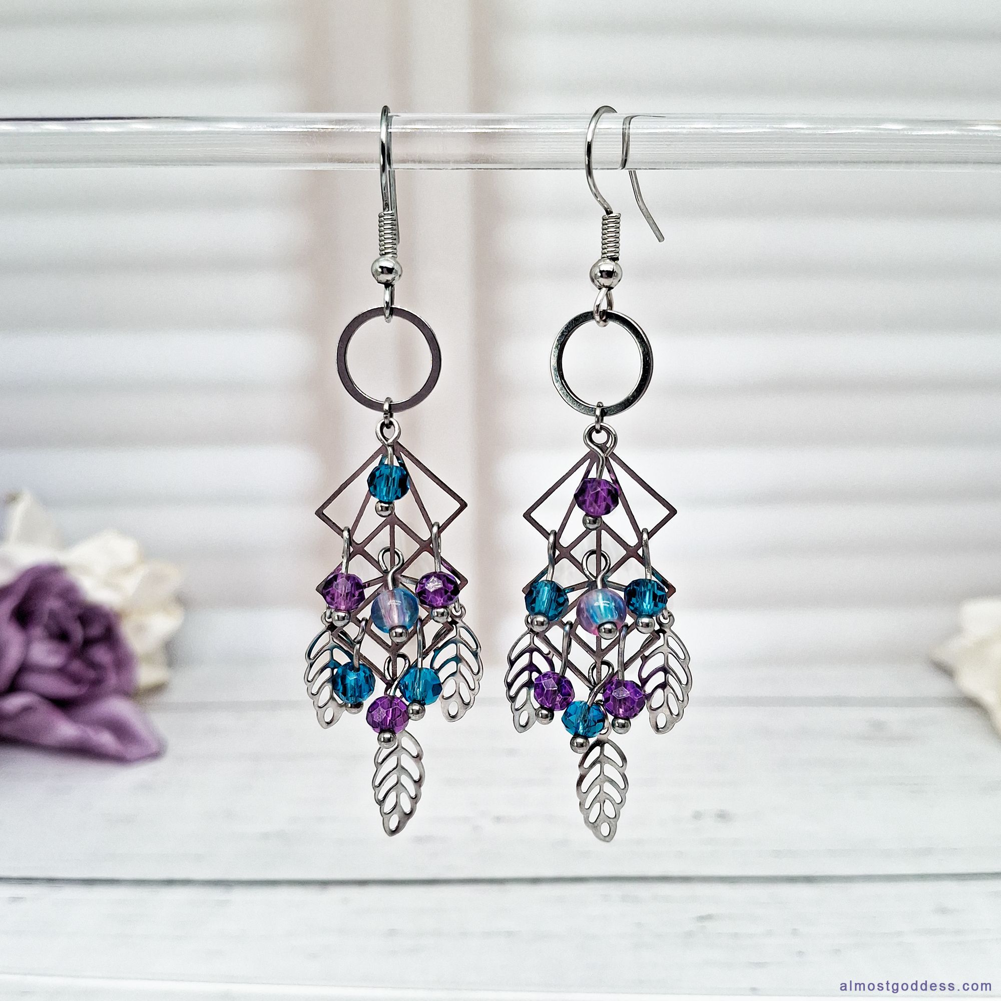 Bohemian dreamcatcher chandelier earrings in silver-tone stainless steel. Features a geometric diamond frame with dangling leaf charms and faceted blue and purple glass beads. Hypoallergenic statement jewelry for women.