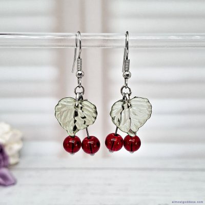Red cherry dangle earrings with green acrylic leaf charms and glass bead berries. Silver-tone stainless steel fruit drop earrings on fishhook wires, hypoallergenic fun statement jewelry for sensitive ears