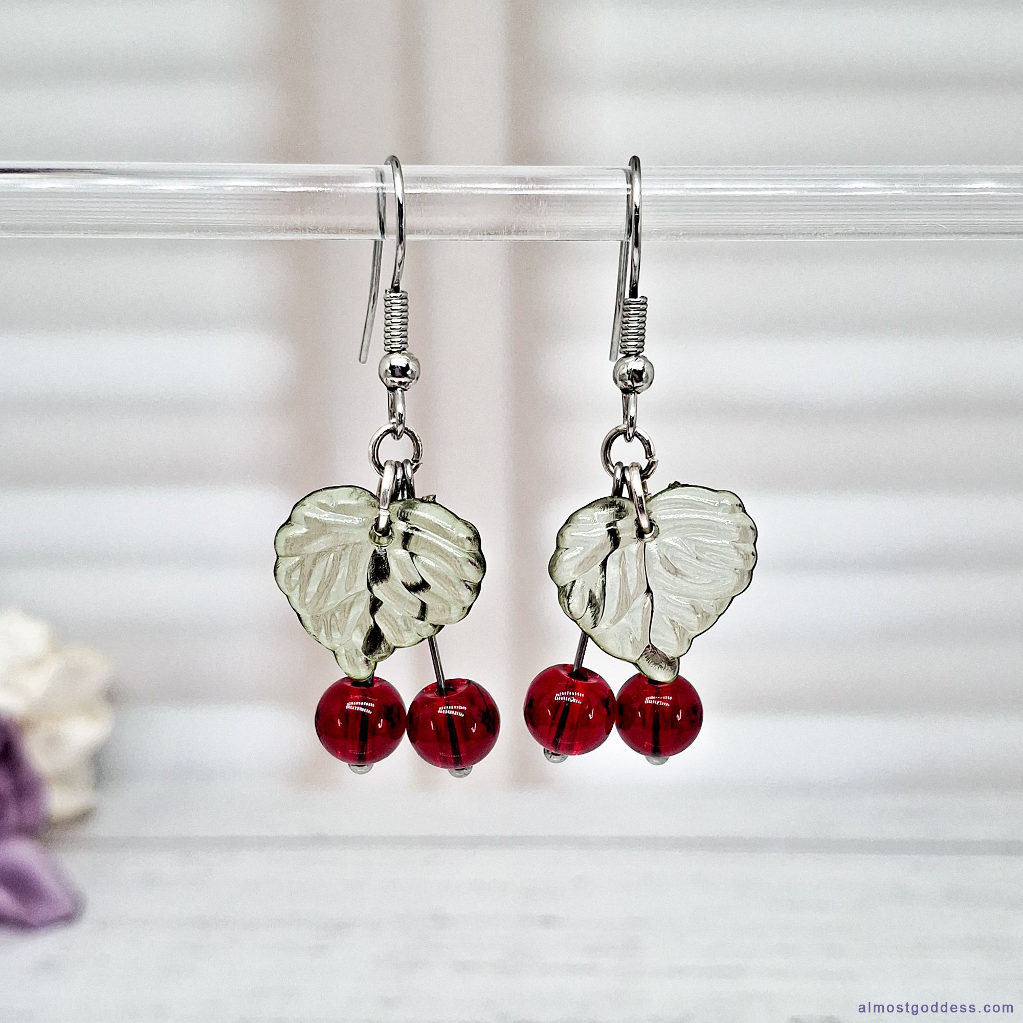 Red cherry dangle earrings with green acrylic leaf charms and glass bead berries. Silver-tone stainless steel fruit drop earrings on fishhook wires, hypoallergenic fun statement jewelry for sensitive ears