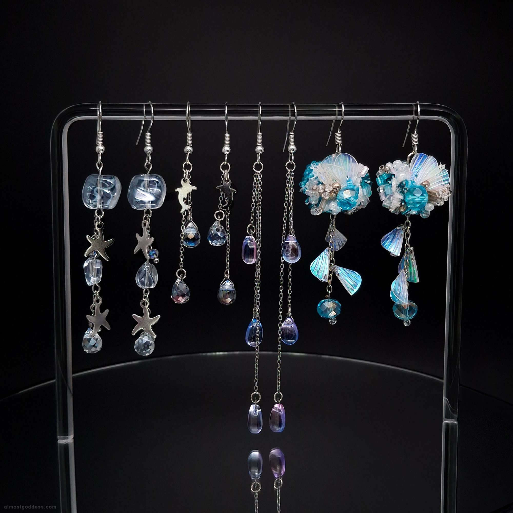Handmade water themed dangle earrings set with beach and ocean motifs. Four pairs of hypoallergenic stainless steel earrings featuring marine life charms, iridescent shells, and faceted glass beads in aqua colors