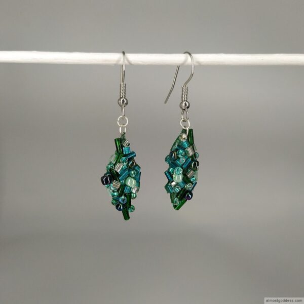 Handmade embroidered green leaf dangle earrings with mixed green and teal seed beads. Stainless steel fishhook drop earrings featuring intricate beadwork and leaf-shaped design for sensitive ears