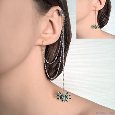 Woman wearing silver ear cuff with long draping chains and green beaded spider dangle earrings. Gothic style asymmetrical jewelry with hanging chains and crystal spider