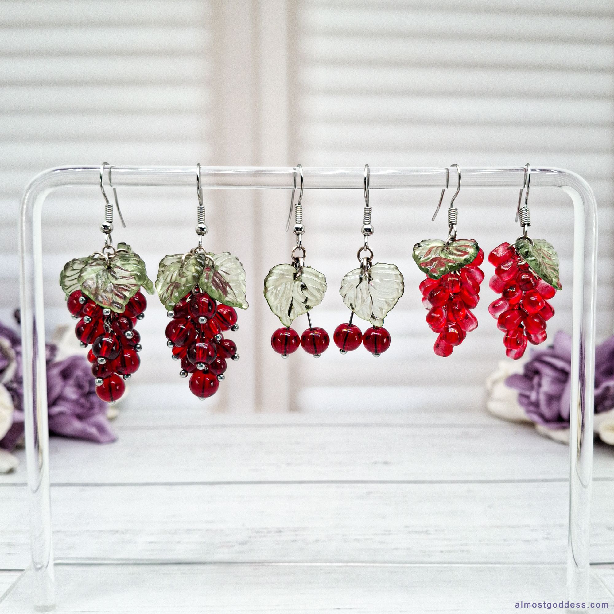 Handmade red berry dangle earrings collection with cherry, pomegranate and currant designs on clear acrylic stand for everyday wear. Stainless steel hooks for sensitive ears