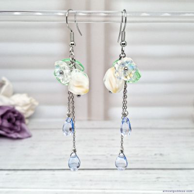 Delicate handmade floral dangle earrings featuring green leaf accents and blue teardrop beads on silver hooks for summer wear