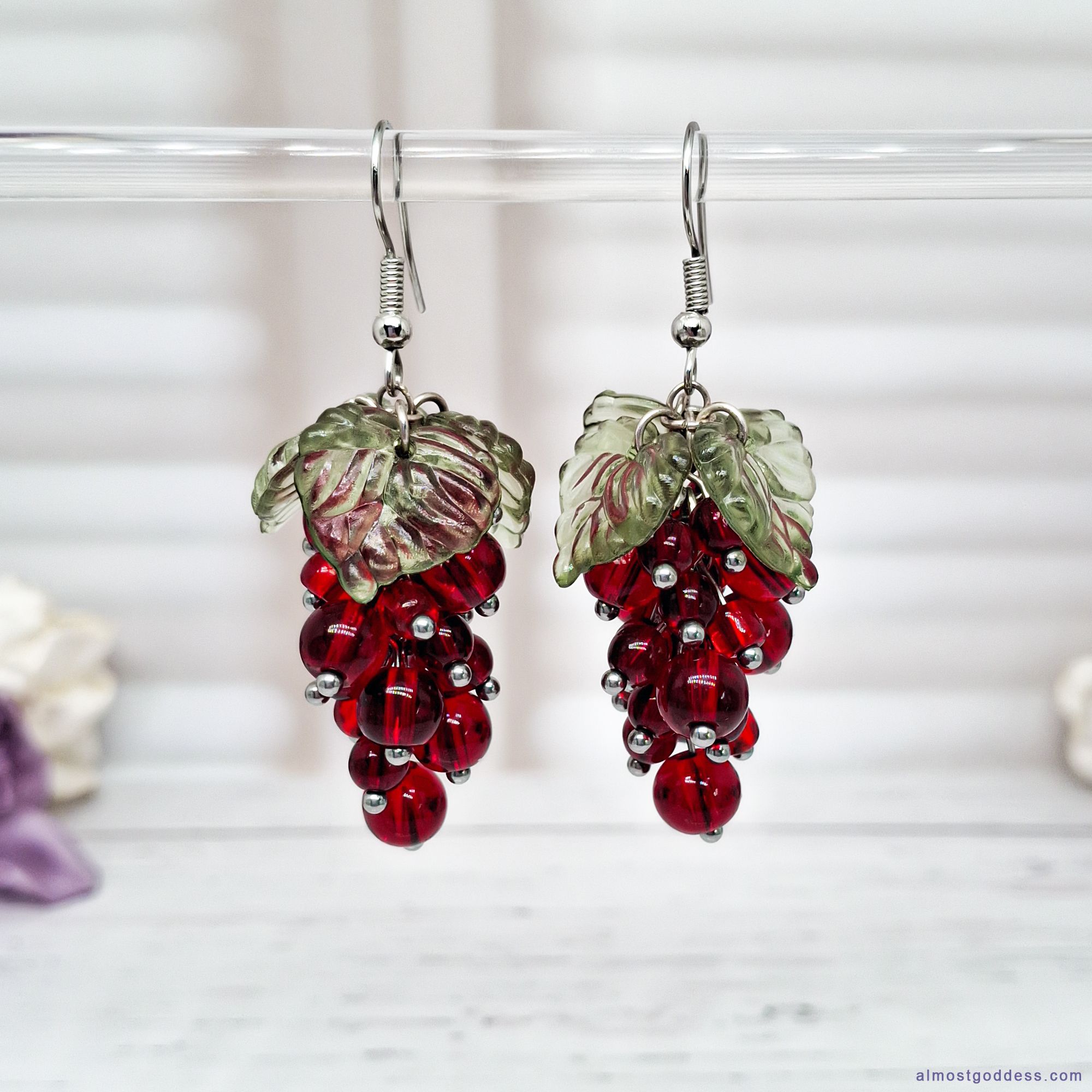 Red currant cluster dangle earrings with glass bead berries and green acrylic leaf charms. Stainless steel fruit drop earrings on fishhook wires, featuring handmade grape-style jewelry with hypoallergenic hooks for sensitive ears