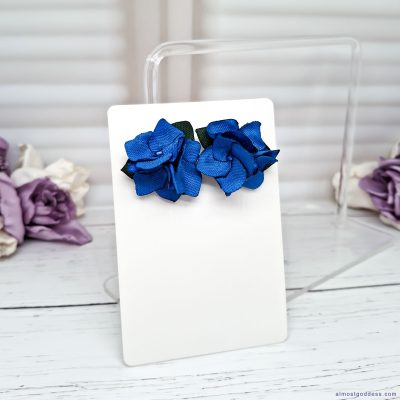 Handmade blue flower stud earrings closeup showing satin ribbon petals and green fabric leaves detail