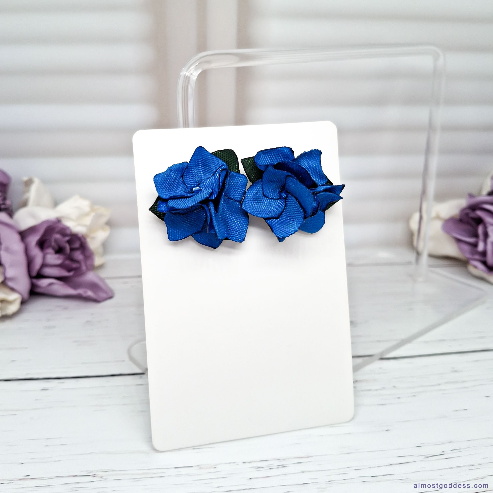 Handmade blue flower stud earrings closeup showing satin ribbon petals and green fabric leaves detail